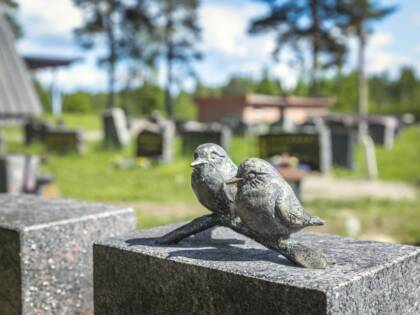 Hautakiven päällä pienessä veistoksessa on kaksi pientä lintua oksalla.