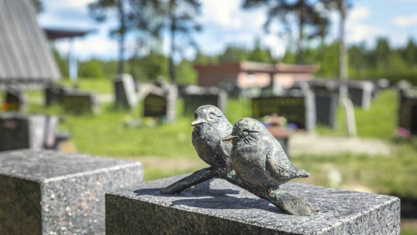Hautakiven päällä pienessä veistoksessa on kaksi pientä lintua oksalla.
