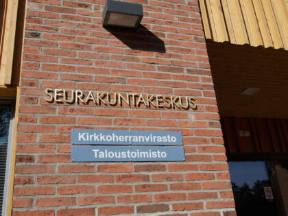 Punatiiliseen ulkoseinään kiinnitetyissä kylteissä lukee Seurakuntakeskus ja Kirkkoherranvirasto.
