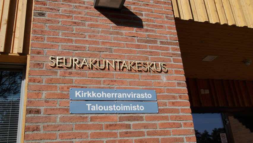 Punatiiliseen ulkoseinään kiinnitetyissä kylteissä lukee Seurakuntakeskus ja Kirkkoherranvirasto.