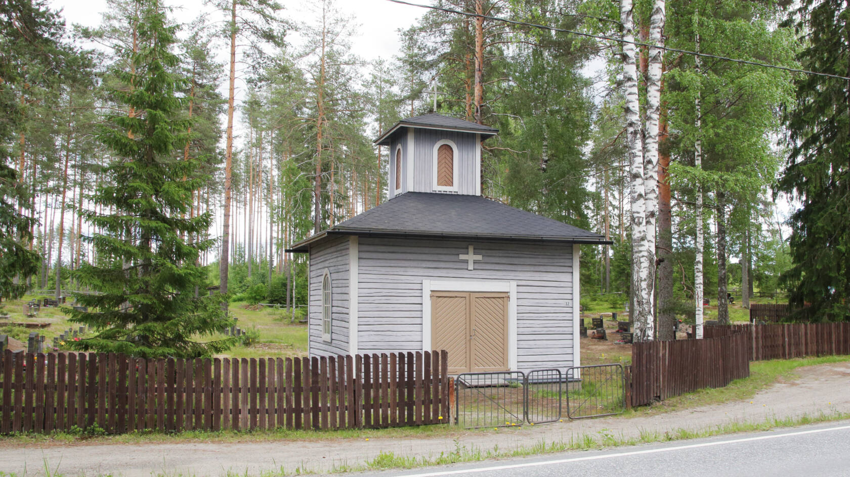 Tien vieressä pieni vaaleanharmaa ja hirsirakenteinen kappeli, jossa on pieni torni.