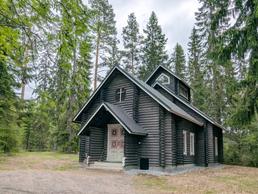 Kuusien ja pihlajien keskellä on harmaista pyöröhirsistä valmistettu kappeli.
