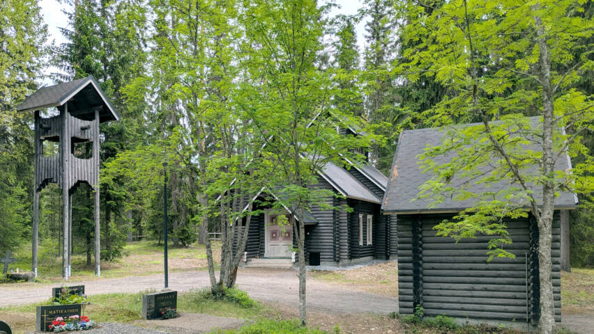 Hautausmaan vieressä harmaasta pyöröhirrestä tehdyt kellotorni, kappeli ja portti.
