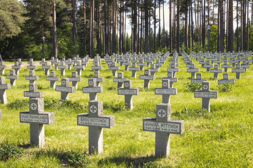 Kiviristit, joihin on kirjoitettu sankarivainajien nimet, seisovat nurmikolla tasaisin välein. Taustalla on mäntymetsää.