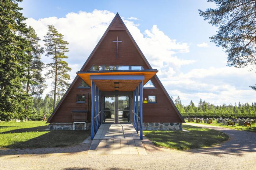 Hautausmaan keskellä sijaitsevan kolmiomuotoisen kappelin terävä harjakatto ulottuu lähellee maata.