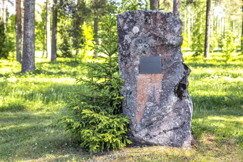 Pysty, karkeasti muotoiltu kivi, johon on kiinnitetty metallinen tekstilaatta.
