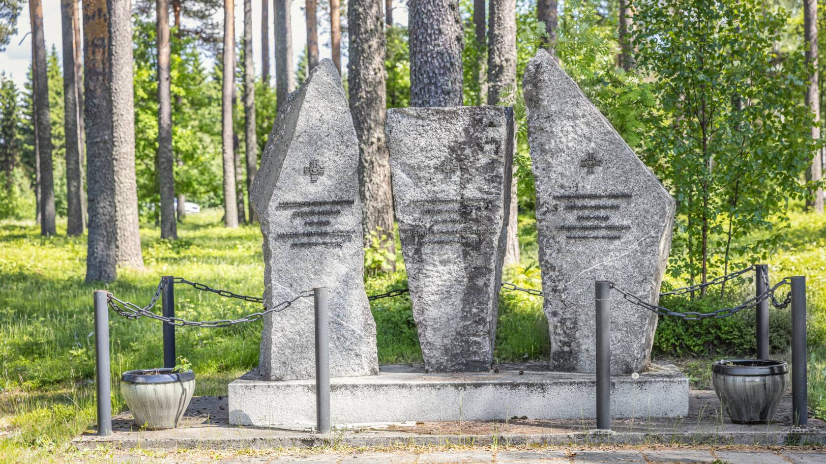 Kolmesta pystyssä seisovaa kivenlohkaretta, joihin on kiinnitetty metallimerkit ja tekstiä metallikirjaimin.