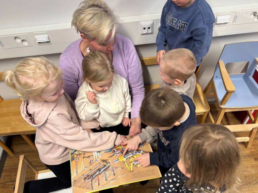 Lapset tutkivat ohjaajan kanssa kirjaa.