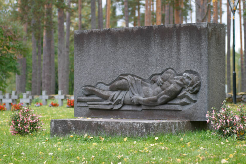 Suorakulmaisen kivipaaden alaosassa on lepäävä Kristus-hahmo. Muistomerkin ympärillä on sankarihautoja ruohikolla.
