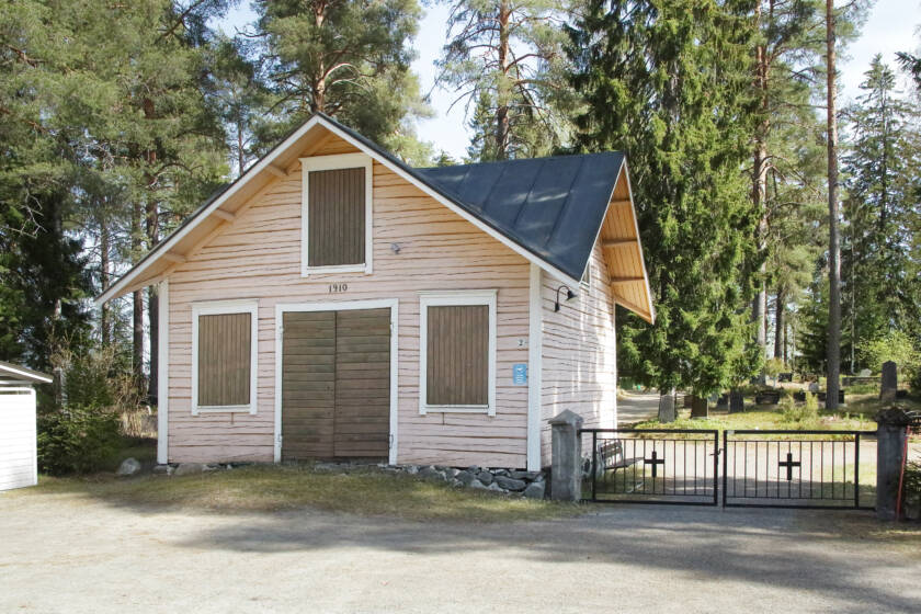 Vanha hirsinen paarihuone ja sen vieressä metalliportti hautausmaalle.