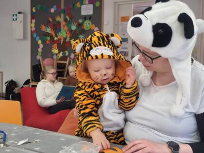 Tiikeriasuinen pienokainen istuu panda-asuisen äidin sylissä.