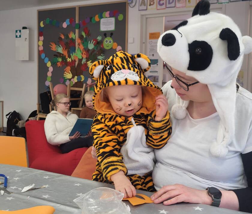 Tiikeriasuinen pienokainen istuu panda-asuisen äidin sylissä.