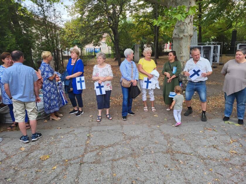 Pihalla, puiden edessä, seisoo rivissä ihmisiä pienet Suomen liput käsissään.