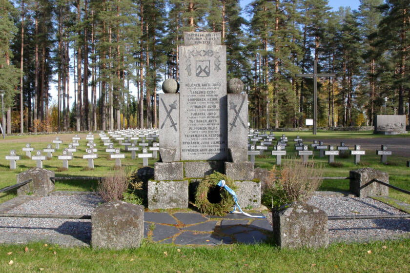 Nurmikentällä on pieniä kivisiä ristejä, ja niiden edessä kivimuistomerkki, johon on kaiverrettu nimiä ja koristekuvioita. Sen eteen on tuotu havuseppele.