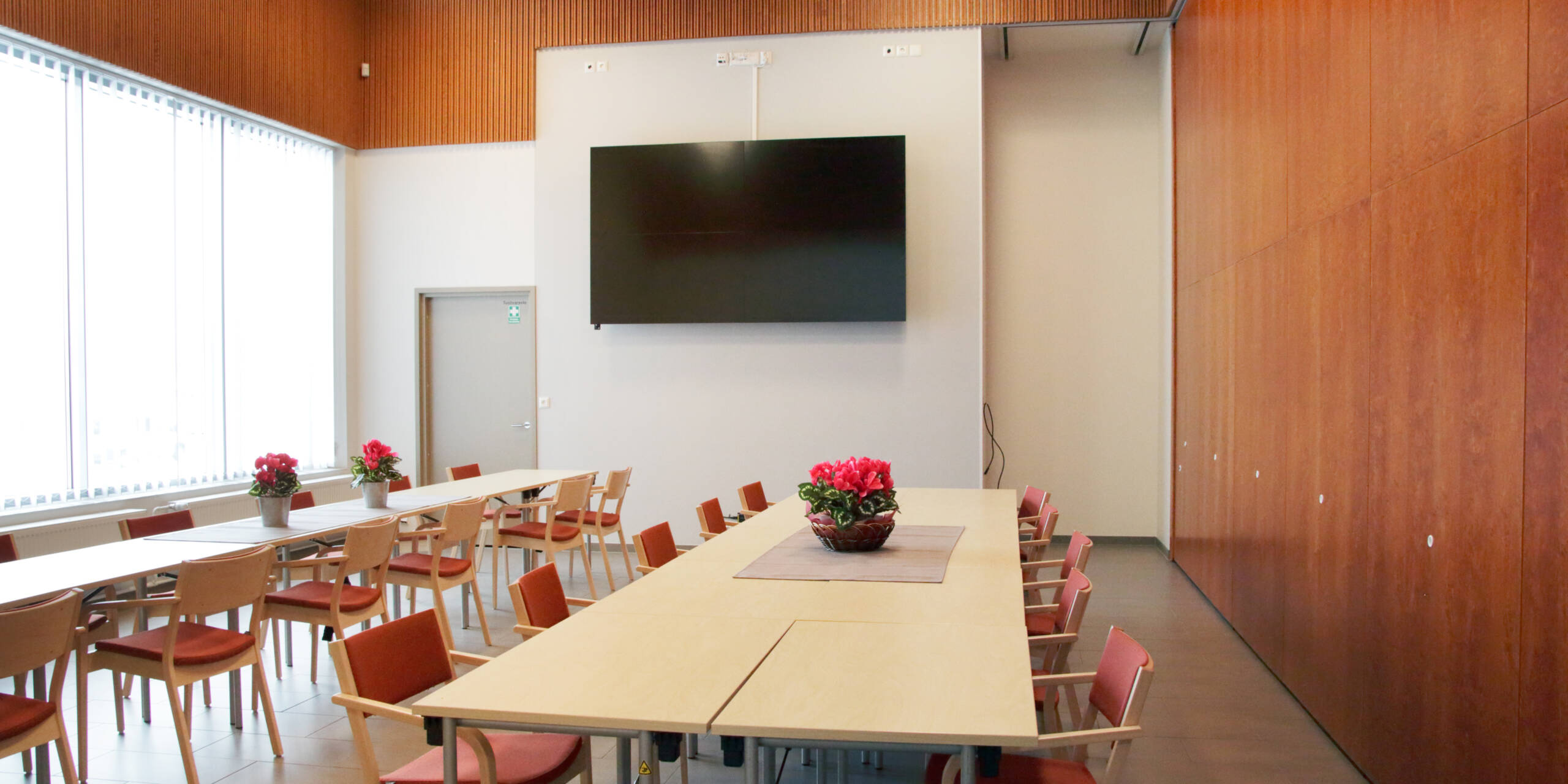 Seurakuntakeskuksen pieni sali on erotettu vedettävällä seinämällä isosta salista. Takaseinällä on iso näyttö, ja sen edessä pöytiä ja tuoleja.